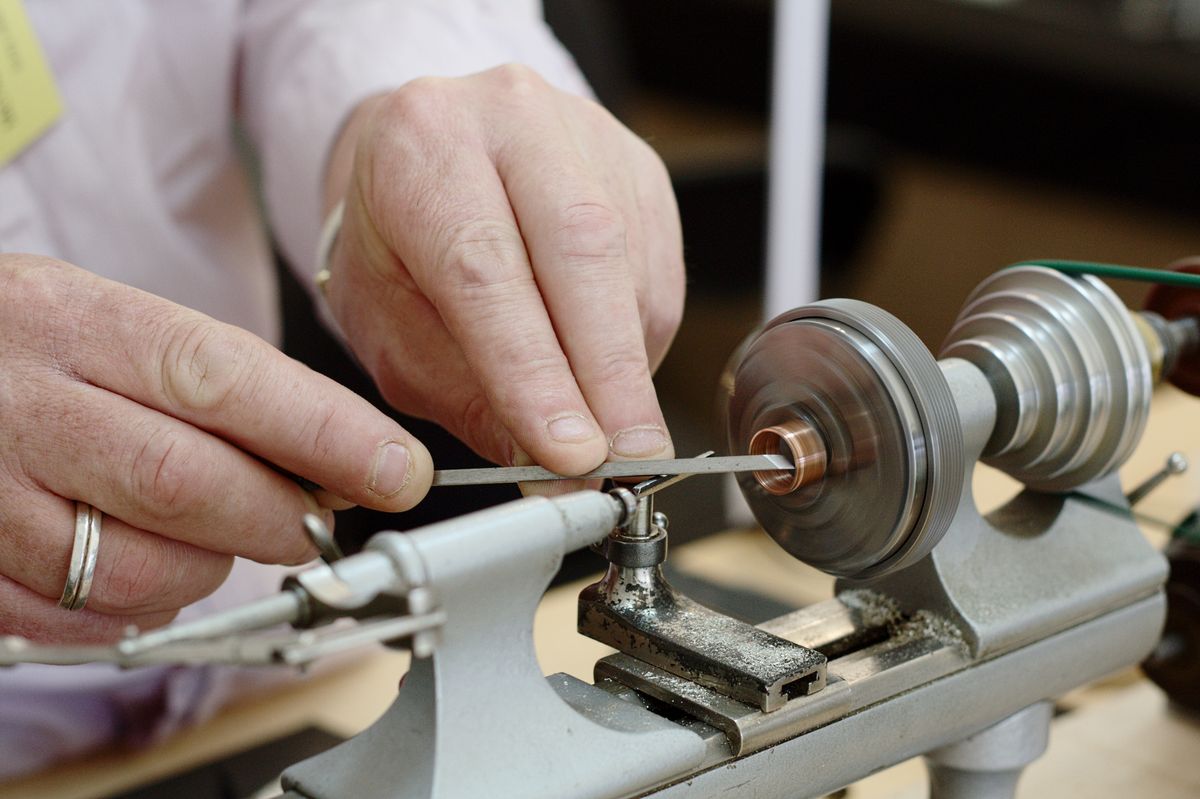 Handen van een uurwerkmaker die een klein onderdeel afwerken op een draaibank